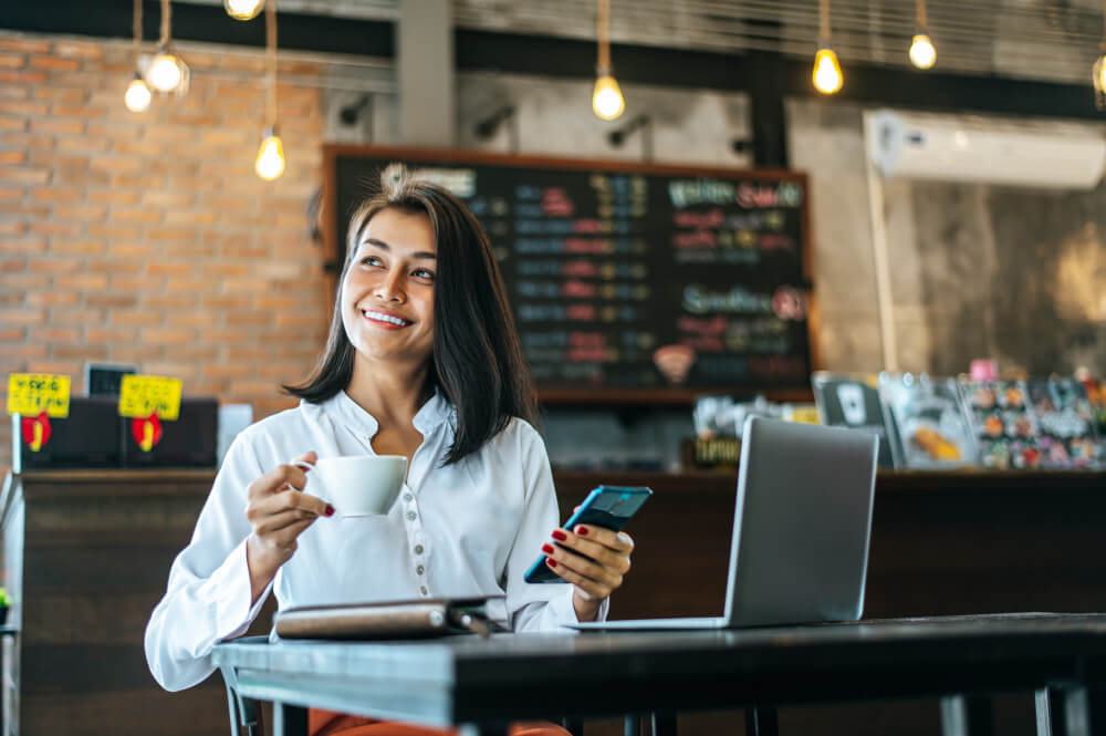 Woman sitting happily working with smartphone coffee shop notebook